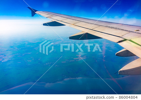 View from the airplane window at a beautiful blue clear sky, earth, sea and the airplane wing View from the airplane window at a beautiful blue clear sky, earth, sea and the airplane wing 86004804