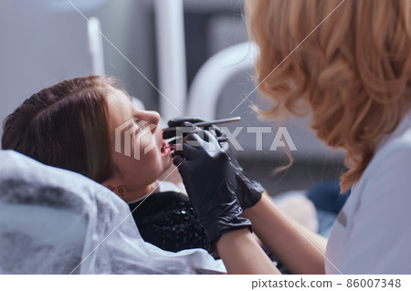 Caucasian young child girl sitting in medical chair while dentist fixing teeth at dental clinic using dental tools instruments, close-up photo of face. professional medical specialist. 86007348