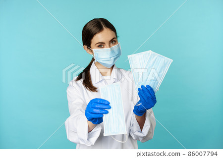 Portrait of medical worker, woman doctor in suggesting face masks from covid-19 pandemic, standing in hospital uniform over torquoise background 86007794