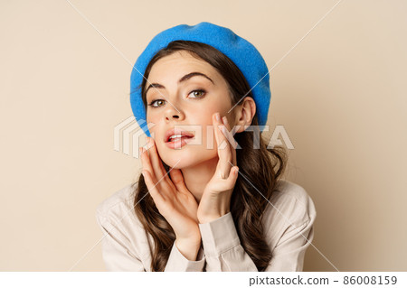 Close up portrait of young beatufiul woman looking in mirror and fixing her makeup, touching soft clear skin, standing over beige background Close up portrait of young beatufiul woman looking in mirror and fixing her makeup, touching soft clear skin, standing over beige background 86008159
