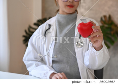 Asian female doctor holding red heart shape in hand. Healthcare and medical concept. Asian female doctor holding red heart shape in hand. Healthcare and medical concept. 86008662