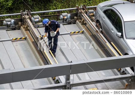 Male worker performing regular inspection and maintenance work on the pallet of the mechanical parking lot 86010869