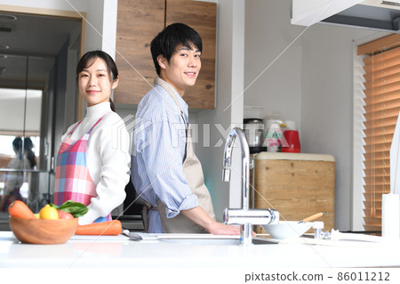A young couple looking at the camera back to back in the kitchen A young couple looking at the camera back to back in the kitchen 86011212