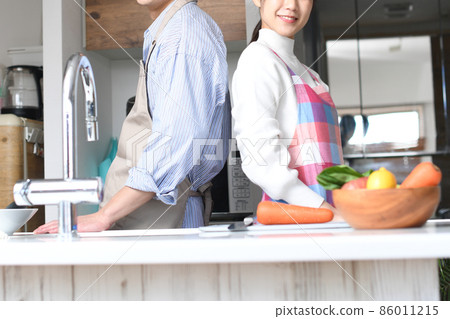 A young couple looking at the camera back to back in the kitchen A young couple looking at the camera back to back in the kitchen 86011215