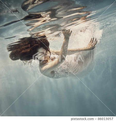 A girl in a white dress with dark hair swims underwater as if flying 86013057