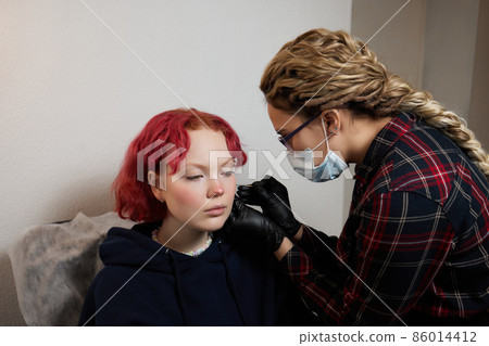 A beautician makes a puncture of the earlobe with a disposable device in a beauty salon. Ear piercing lobe. A beautician makes a puncture of the earlobe with a disposable device in a beauty salon. Ear piercing lobe. 86014412