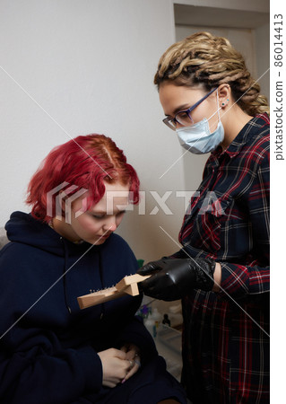 A beautician makes a puncture of the earlobe with a disposable device in a beauty salon. Ear piercing lobe. A beautician makes a puncture of the earlobe with a disposable device in a beauty salon. Ear piercing lobe. 86014413