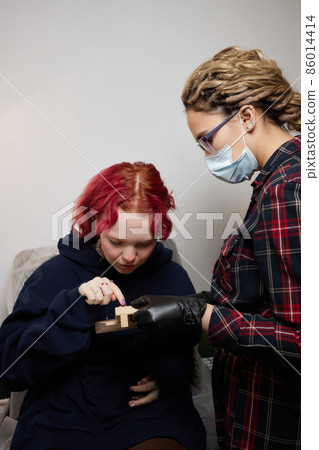 A beautician makes a puncture of the earlobe with a disposable device in a beauty salon. Ear piercing lobe. A beautician makes a puncture of the earlobe with a disposable device in a beauty salon. Ear piercing lobe. 86014414