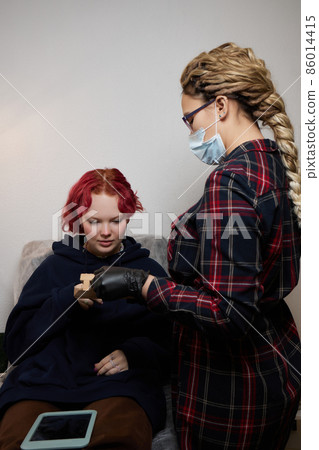 A beautician makes a puncture of the earlobe with a disposable device in a beauty salon. Ear piercing lobe. A beautician makes a puncture of the earlobe with a disposable device in a beauty salon. Ear piercing lobe. 86014415