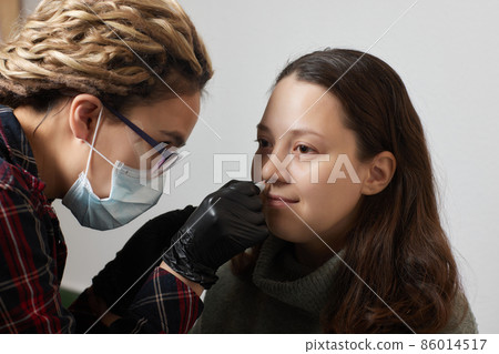Closeup of a young woman's visage with piercing septum hanging from her nose. 86014517