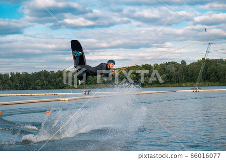 Confident male wakeboarder jumping over water surface on lake on summer day Confident male wakeboarder jumping over water surface on lake on summer day 86016077