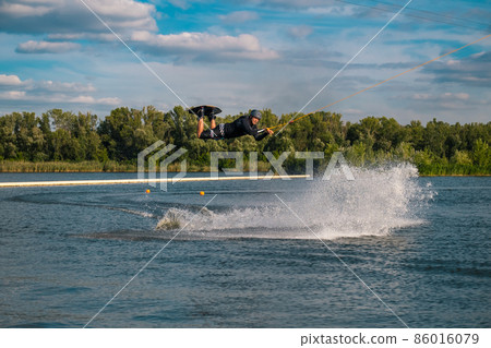 Man practicing tricks on wakeboard, jumping over water holding on tow rope Man practicing tricks on wakeboard, jumping over water holding on tow rope 86016079
