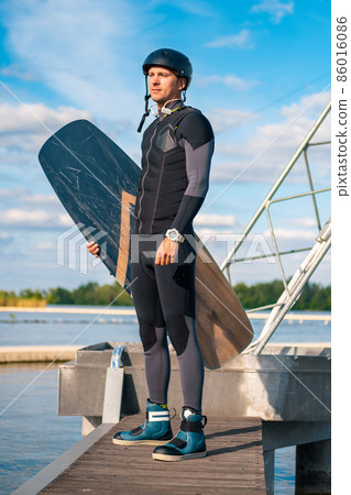 Full length portrait of wakeboarder with board in hand standing on pier Full length portrait of wakeboarder with board in hand standing on pier 86016086