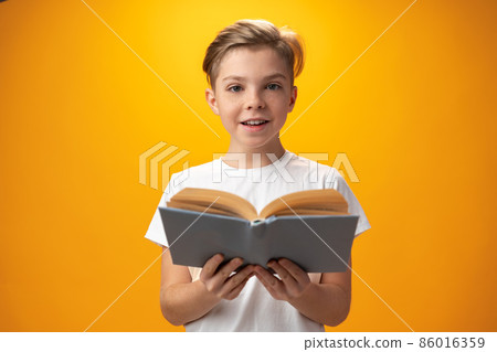 Little schoolboy holding a book against yellow background Little schoolboy holding a book against yellow background 86016359