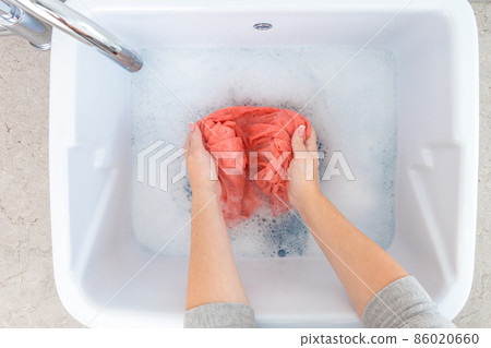 Female hands washing color clothes in sink Female hands washing color clothes in sink 86020660