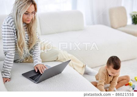 mom working at home on sofa writing an email while child playing on floor. 86021558