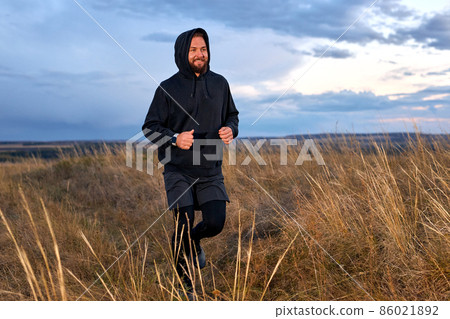 Handsome Caucasian Male Running Through the field. Man Wearing Black sportive wear 86021892