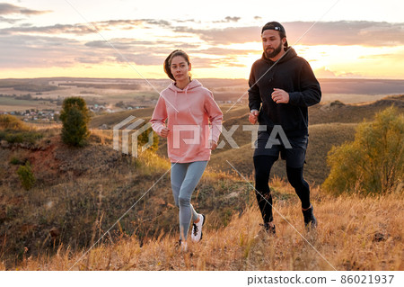 man and woman running at sunset or sunrise along field mountains, morning jogging 86021937