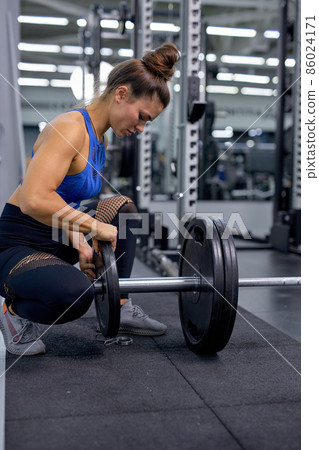 Athletic woman working out in gym. Female athlete adjusts weight for lifting. Athletic woman working out in gym. Female athlete adjusts weight for lifting. 86024171