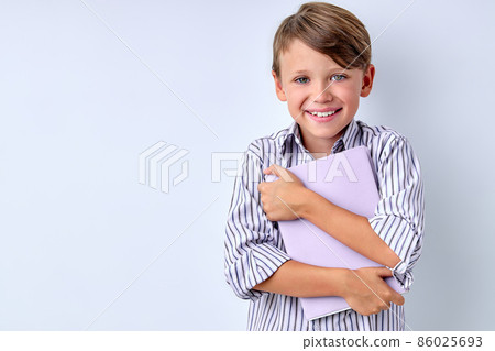 Portrait of happy kid holding book, hugging it, stand isolated over white background studio. 86025693