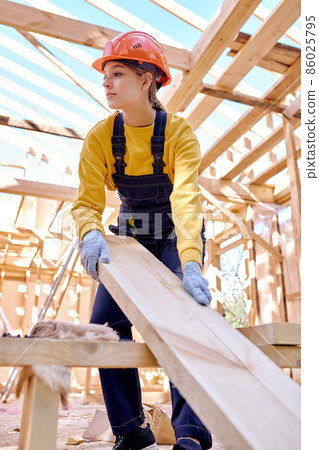 female constructor wearing helmet while preparing frame, dragging wooden beam female constructor wearing helmet while preparing frame, dragging wooden beam 86025795