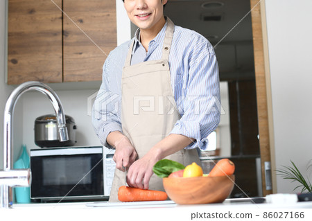 A young black-haired man in an apron cooking in the kitchen 86027166
