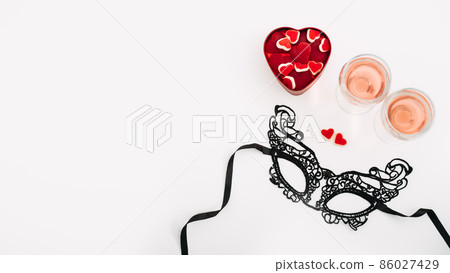 Valentines Day Festive banner with black lace mask, two glasses of rose wine and two red heart shape candies on white table. Valentine Day, flirting, romance, dating concept, copy space 86027429