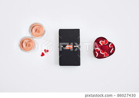 Valentines Day gift wrapping, package. Valentines Day gift background with black craft gift box with text I Love you, wine glasses and two red paper hearts Valentines Day gift wrapping, package. Valentines Day gift background with black craft gift box with text I Love you, wine glasses and two red paper hearts 86027430
