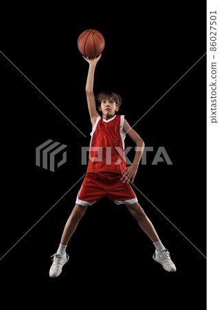 Full-length studio shot of basketball player in motion, jumping and throwing ball isolated over black background 86027501