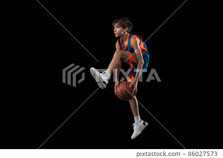 Full-length studio shot of young boy, teenager, basketball player in motion, training isolated over black background 86027573