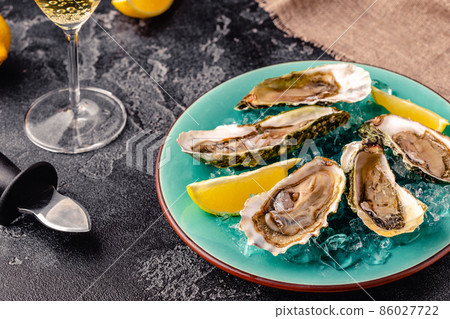 Opened fresh oysters on a blue plate, served with lemon and ice. Opened fresh oysters on a blue plate, served with lemon and ice. 86027722