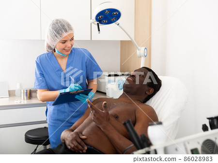 Cosmetician with papers talking to man before procedure in clinic 86028983
