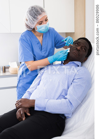 Female beautician injecting facial filler to male client in clinic 86029986