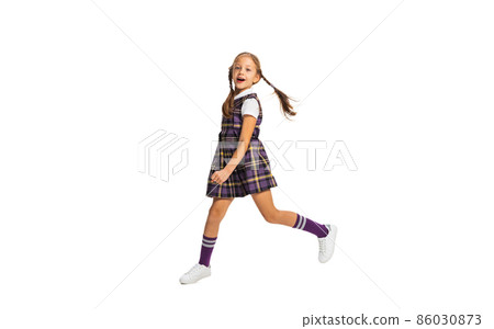 Portrait of cute little girl, pupil in school uniform running isolated on white background. Concept of childhood, emotions, study 86030873