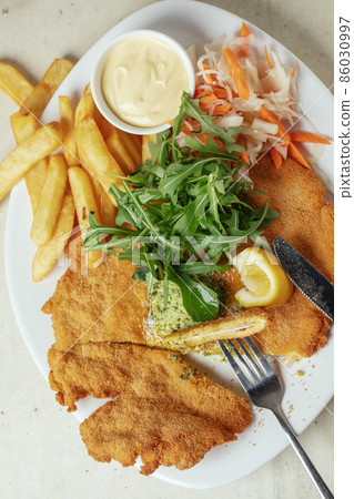 Homemade breaded chicken schnitzel with melting salted butter with herbs french fries , lemon and a fork 86030997