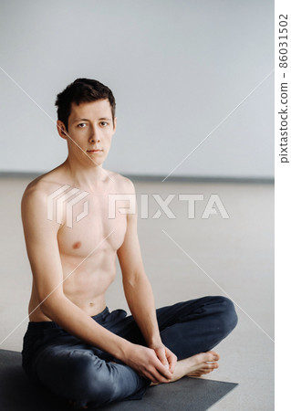 A male athlete with a bare torso is sitting in the gym before training and resting 86031502