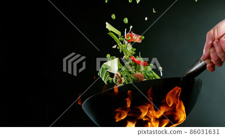 Closeup of chef throwing salmon mix from wok pan in fire. 86031631