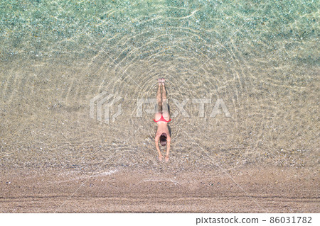 Top, aerial view. Young beautiful woman in a red bikini panties lying and sunbathe in sea water on the sand beach. Drone, copter photo. Summer vacation. View from above. 86031782