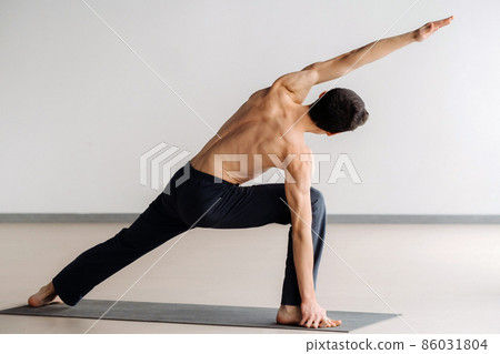 A man with a bare torso trains standing up, doing stretching in the gym A man with a bare torso trains standing up, doing stretching in the gym 86031804