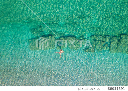 Top view. Young beautiful naked woman in a hat swimming in sea water on sand beach. Drone, copter photo. Summer vacation. View from above. Top view. Young beautiful naked woman in a hat swimming in sea water on sand beach. Drone, copter photo. Summer vacation. View from above. 86031891
