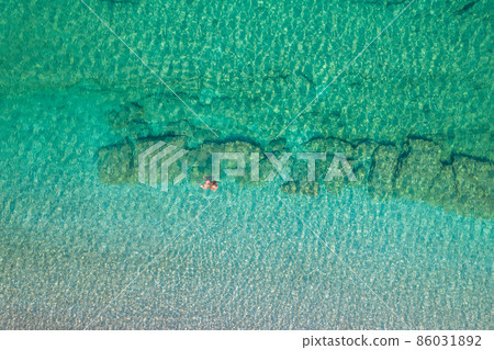 Top view. Young beautiful naked woman in a hat swimming in sea water on sand beach. Drone, copter photo. Summer vacation. View from above. Top view. Young beautiful naked woman in a hat swimming in sea water on sand beach. Drone, copter photo. Summer vacation. View from above. 86031892