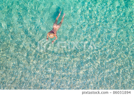Top view. Young beautiful naked woman in a hat swimming in sea water on sand beach. Drone, copter photo. Summer vacation. View from above. Top view. Young beautiful naked woman in a hat swimming in sea water on sand beach. Drone, copter photo. Summer vacation. View from above. 86031894