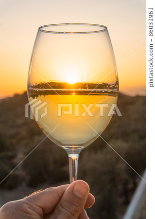 Hand with a glass of white wine on a sunset background. Tasting young white wine in summer Hand with a glass of white wine on a sunset background. Tasting young white wine in summer 86031961