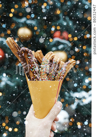 Churros waffles in a hand on the winter snow market. Churros Mexican street food dessert. Fast food sweets, Christmas fair cookies 86032447