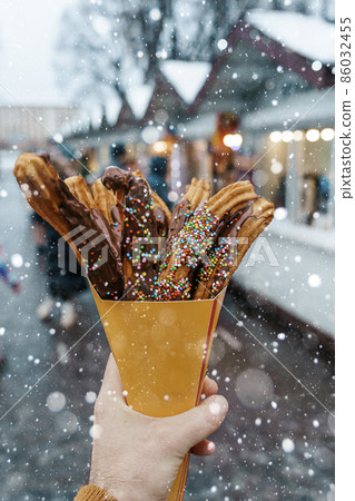 Churros waffles in a hand on the winter snow market. Churros Mexican street food dessert. Fast food sweets, Christmas fair cookies 86032455