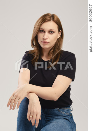 Portrait of young woman in black t shirt and jeans posing over grey background 86032697