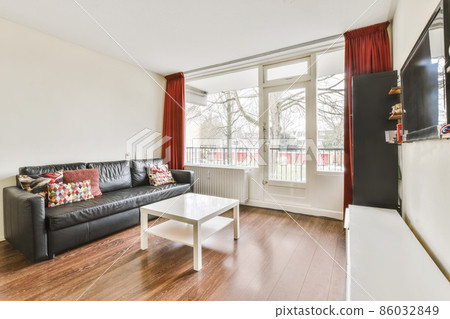 Charming living area with a black leather sofa and a large window 86032849