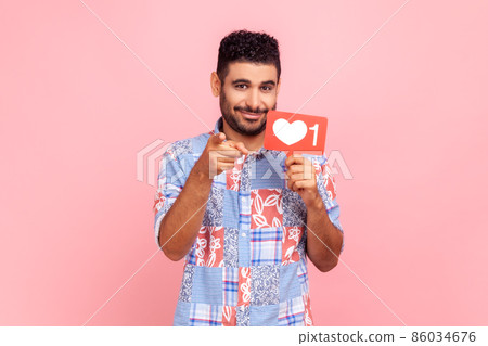 Did you rate my post. Young adult bearded man blogger holding red likes counter sign board and pointing finger at camera, asking to like his content. Indoor studio shot isolated on pink background. 86034676