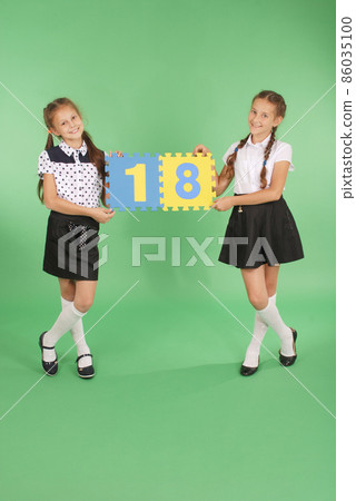 Two school girls hold color board with the number eighteen 86035100