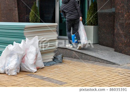 The worker loads building materials and brings them into the entrance for future repairs. Copy space. The worker loads building materials and brings them into the entrance for future repairs. Copy space. 86035391